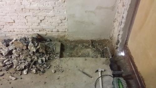 The broken-out floor with rubble and tools while making room for the meter cupboard.