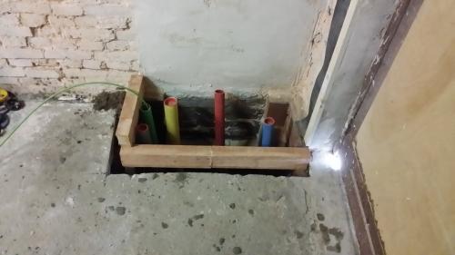 The opening in the floor with service ducts and a surrounding timber frame.