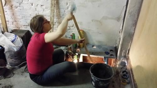 The poured floor beneath the meter cupboard being tamped down with a wooden batten.